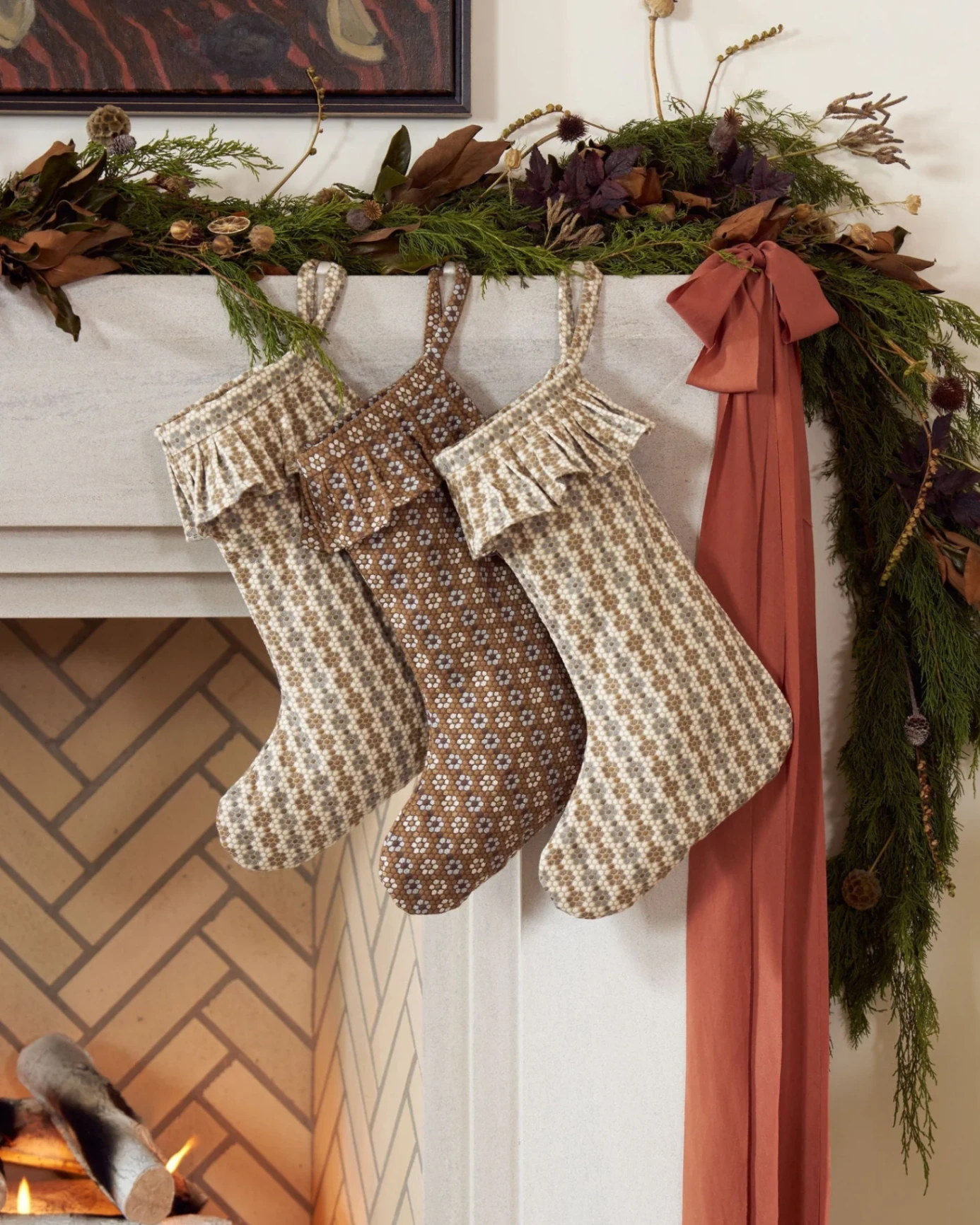 Three Nectar stockings hanging on a mantel with cedar garland and a rust ribbon