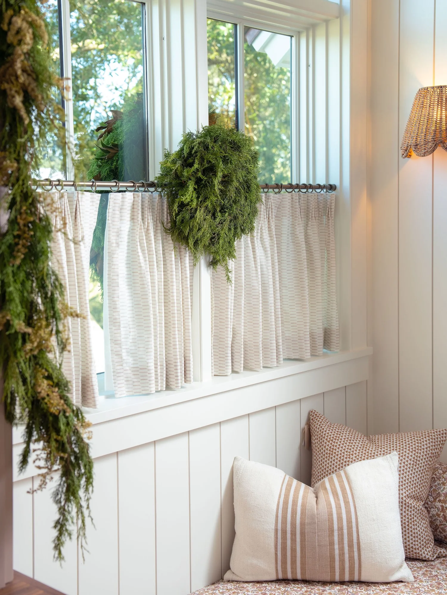 Window seat with cafe curtains, fresh cedar wreath, and pillows