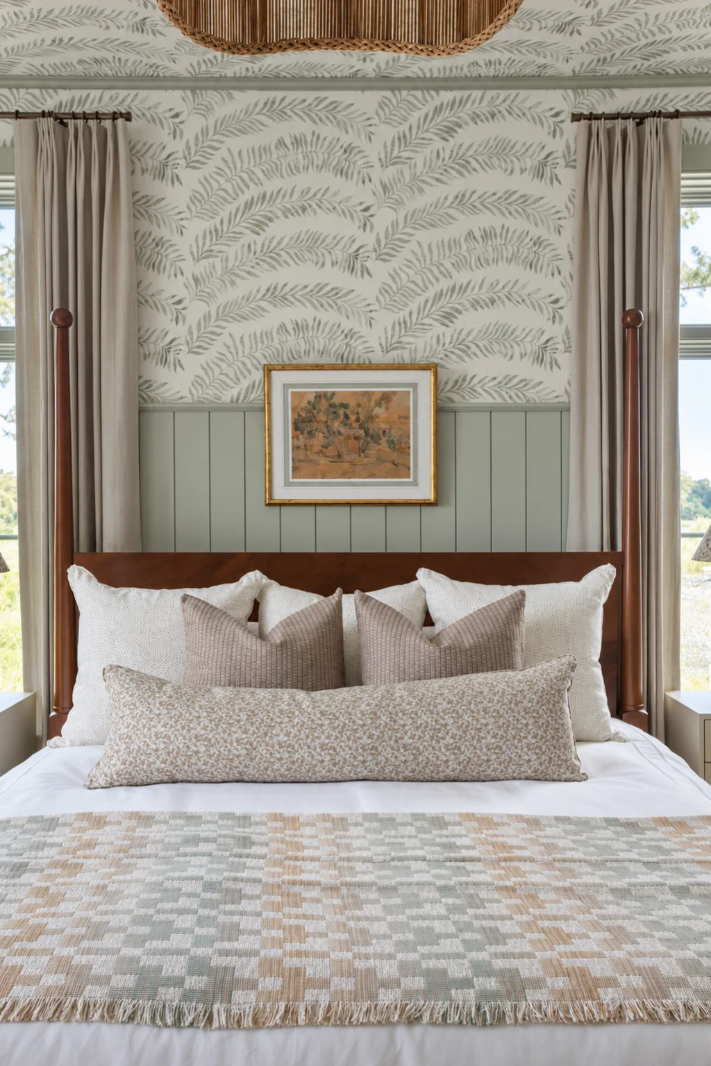 A four-poster bedroom layered with dusty rose woven pillows, a checked throw and soft linen drapery