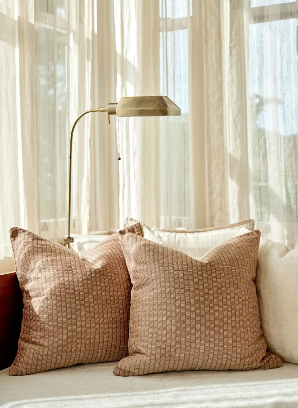 Two Jetty in Punch pillows in a sunlit window seat beside sheer curtains and a brass lamp