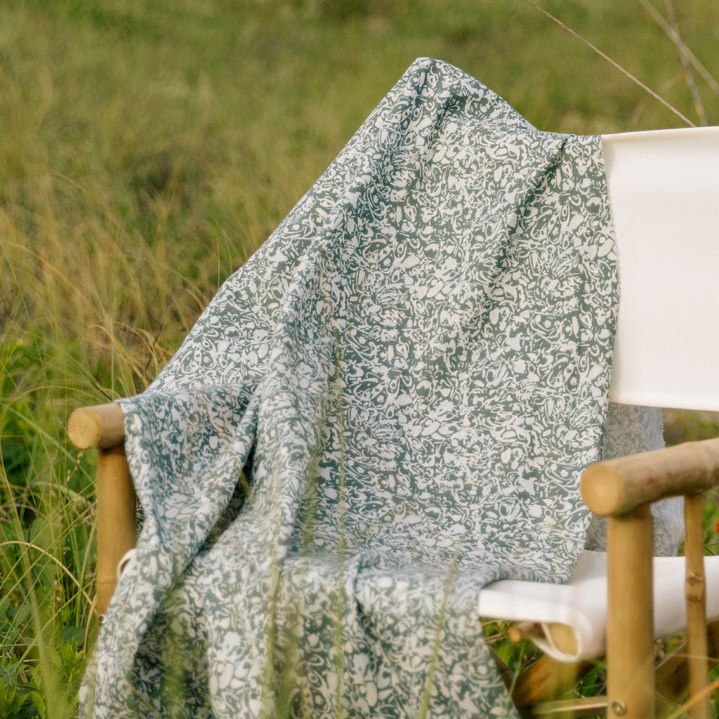 Estuary fabric in peacock draped over a wooden chair in tall grass