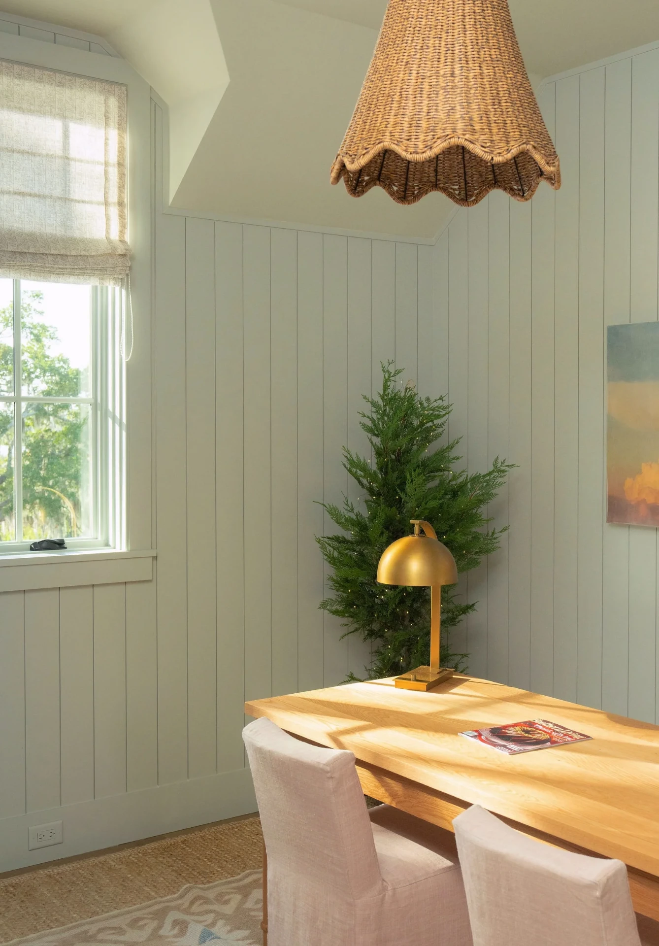 Desk and sage green paneled office with cedar tree and brass lamp